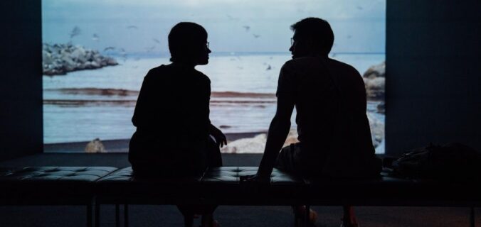 Zwei Menschen sitzen im Gespräch vor einer projizierten Meereslandschaft