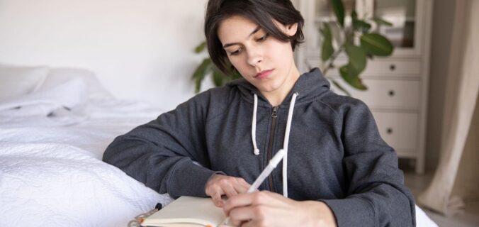Nachdenkliche Person schreibt in einem Notizbuch auf einem kleinen Tisch